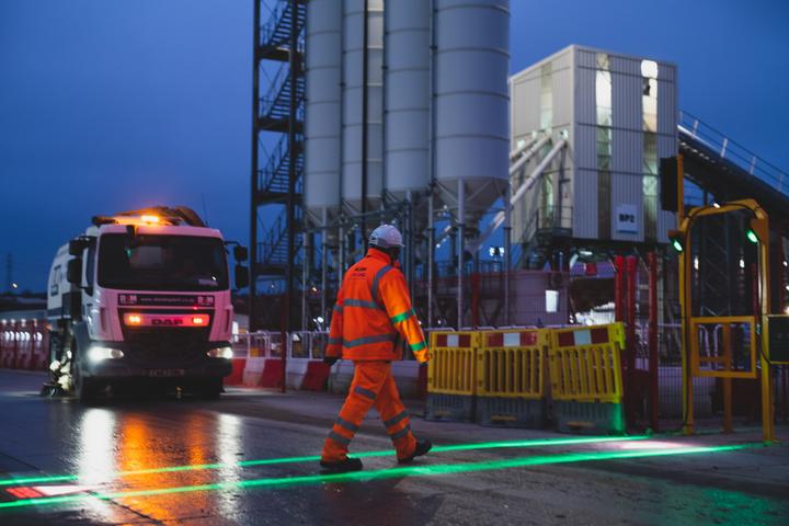 A man crossing an illuminated walkway on a construction site.